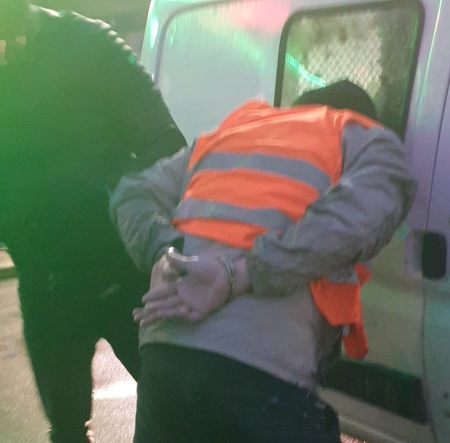 Aresztowano podejrzanego w kajdankach i pomarańczowej kamizelce bezpieczeństwa