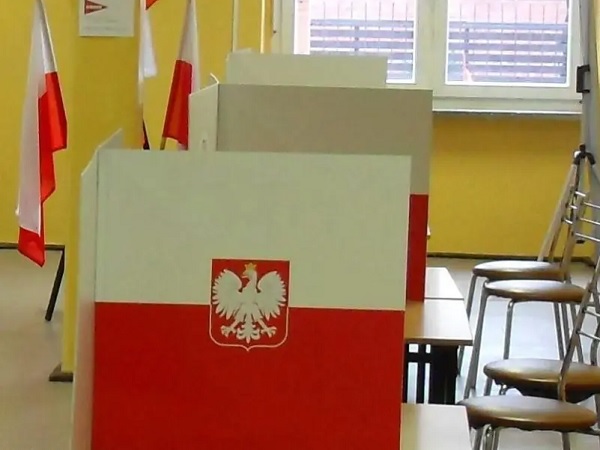 Polski lokal wyborczy z urnami wyborczymi i polskimi flagami.
