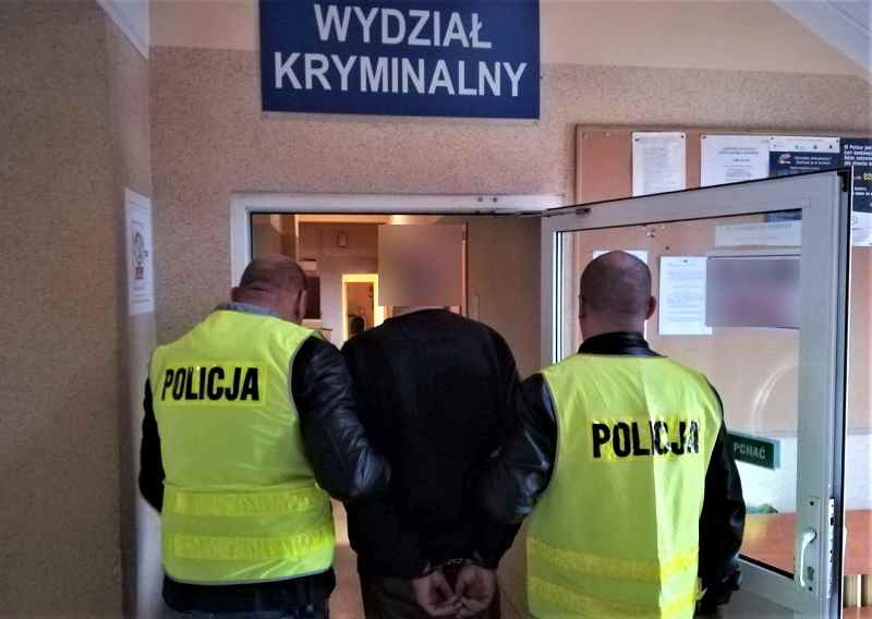 Dwóch polskich policjantów eskortuje podejrzanego do sądu karnego. Widoczne są kamizelki „Policji”.