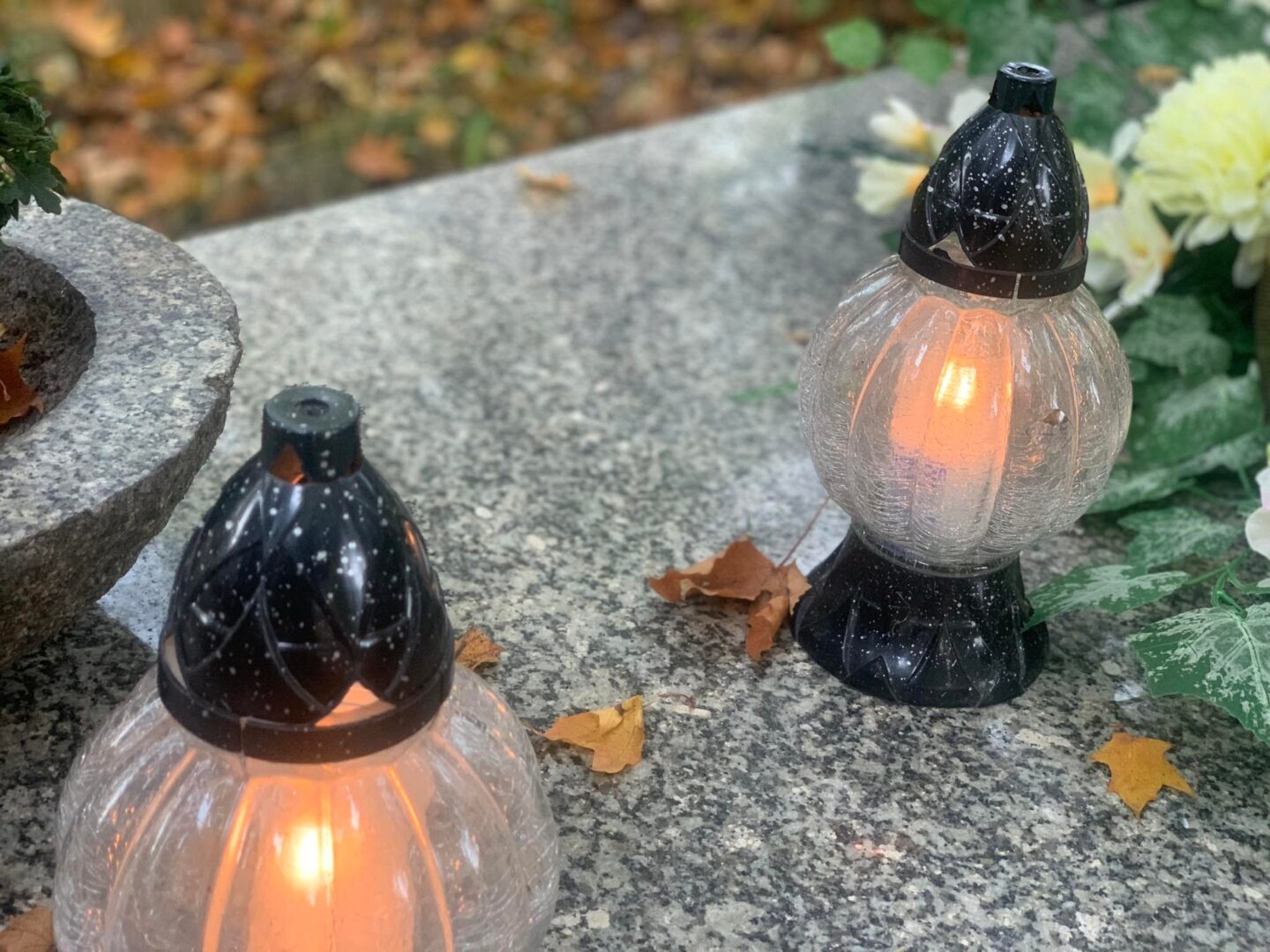 Dwie zapalone świece wotywne na granitowej powierzchni, otoczone jesiennymi liśćmi.