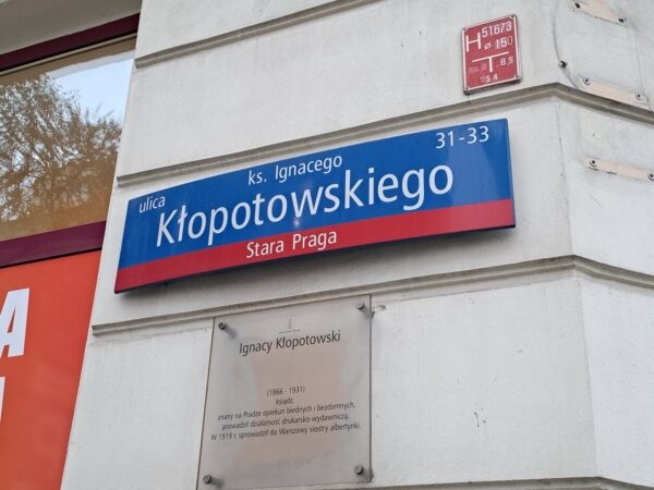 Znak drogowy dla Ks. Ulica Ignacego Kłopotowskiego na Starej Pradze w Warszawie, z tablicą pamiątkową.