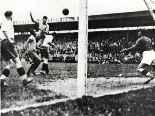 Czarno-białe zdjęcie dramatycznego gola w piłce nożnej, zawodnicy walczą o piłkę przy siatce.