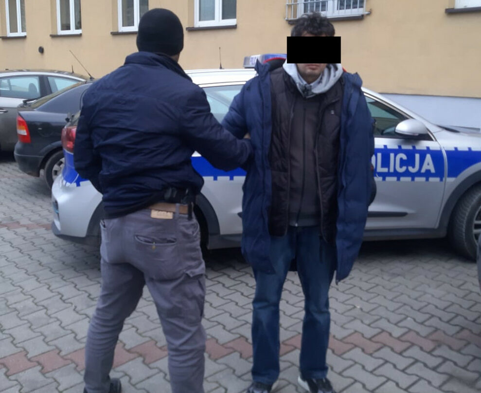 Policjant aresztujący podejrzanego przy radiowozie.