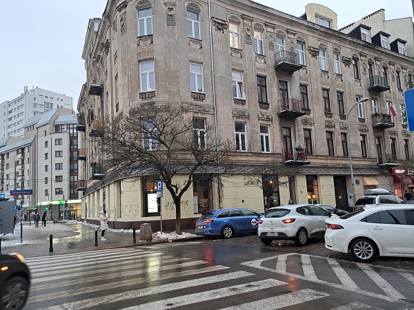 Stary budynek mieszkalny na miejskiej ulicy, samochody zaparkowane wzdłuż krawężnika.