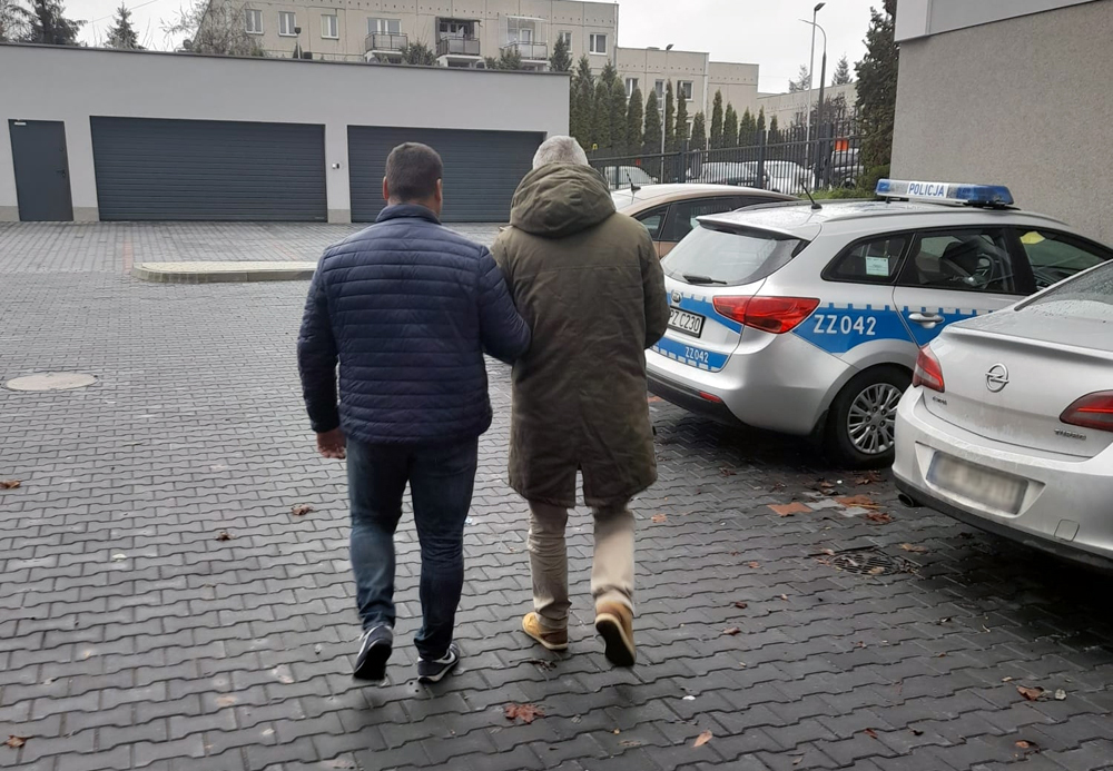 Dwóch mężczyzn w kajdankach odchodzi od radiowozów, na jednym z nich widoczny jest symbol ZZ042.