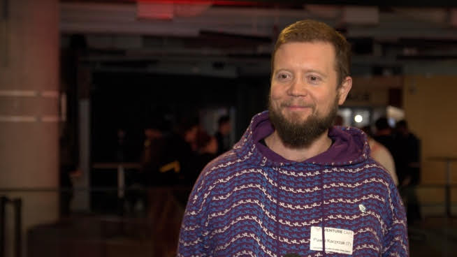 Mężczyzna z brodą w fioletowej bluzie z kapturem w Venture Cafe.