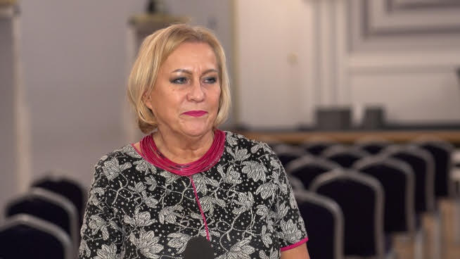 Biznesmenka ubrana w kwiecistą sukienkę i naszyjnik, mówi.