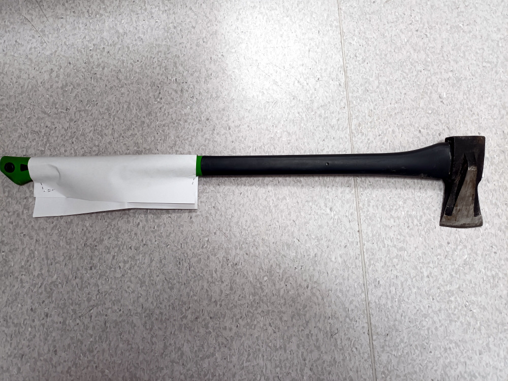 Siekiera do rozłupywania z czarnym uchwytem i zielonymi akcentami, częściowo pokryta białym papierem.