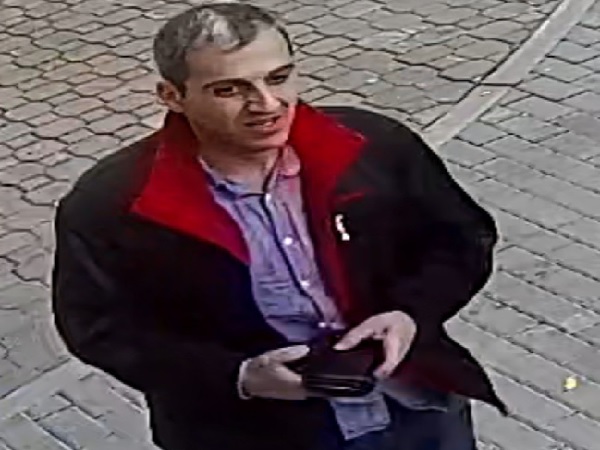 Mężczyzna w ciemnej kurtce z czerwonym kołnierzykiem trzymający portfel