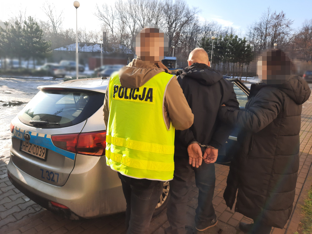 Policjanci zatrzymują podejrzanego w kajdankach w pobliżu radiowozu. POLICJA