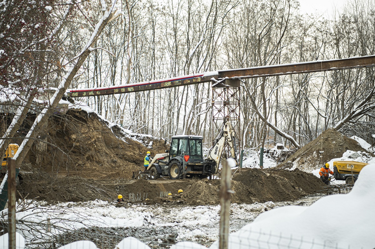 Robotnicy budowlani obsługują koparką podczas zimowej instalacji rurociągów.