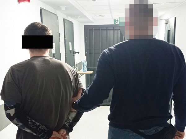 Policjant eskortujący podejrzanego w kajdankach korytarzem.