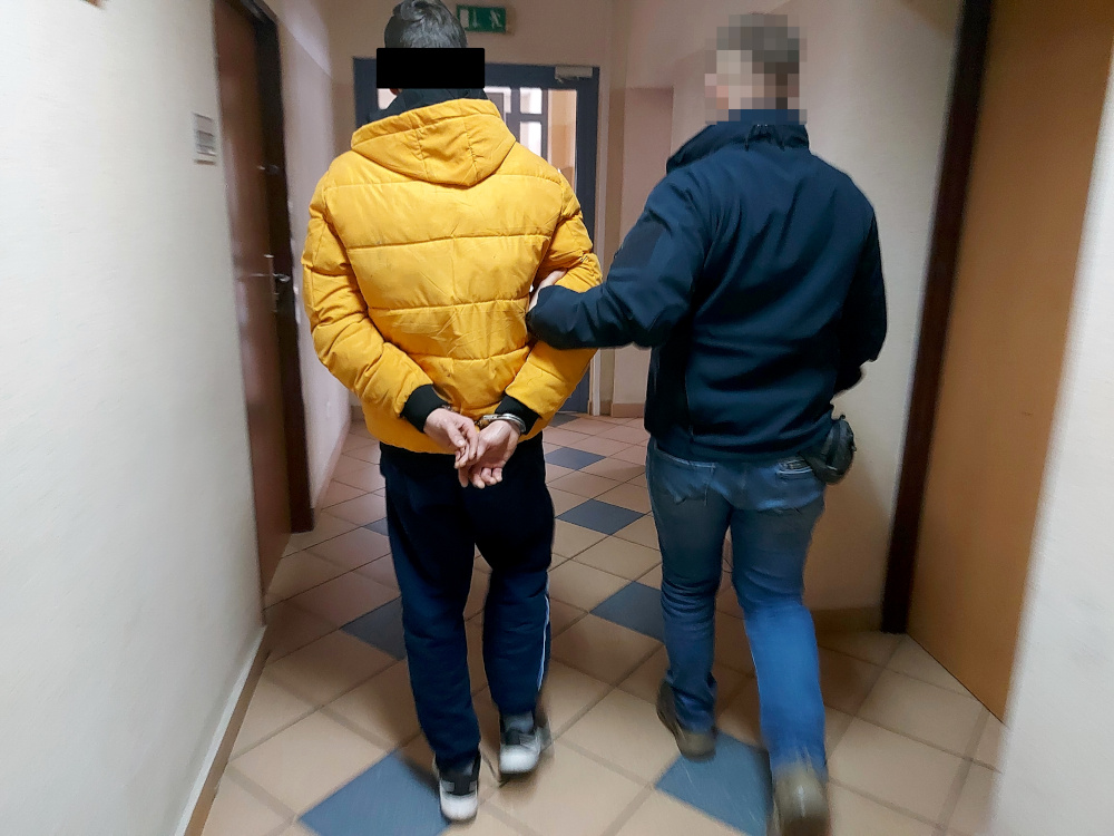 Policjant eskortujący skutego kajdankami podejrzanego korytarzem.