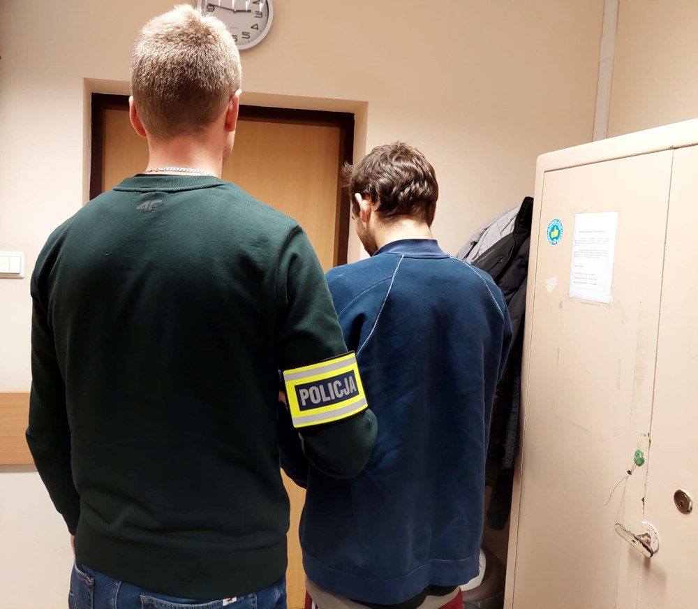 Policjant aresztujący podejrzanego. Widoczna opaska "Policja".