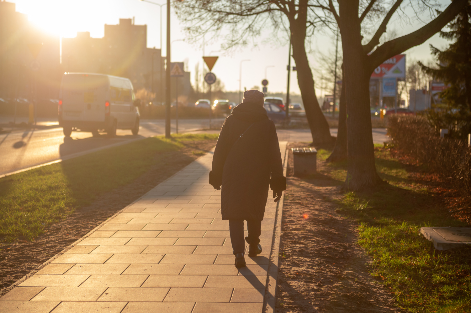 Starsza kobieta spacerująca po chodniku o zachodzie słońca