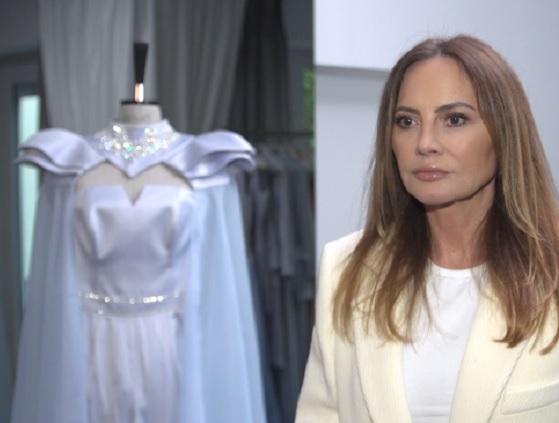 Projektantka mody prezentuje elegancką, jasnoniebieską suknię z peleryną