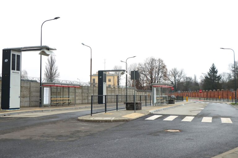 Nowoczesny przystanek autobusowy z wiatami i wyświetlaczami elektronicznymi przy ścianie.