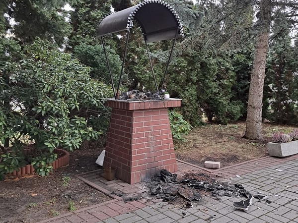 Wypalona ceglana kapliczka z metalowym baldachimem; skutki wandalizmu