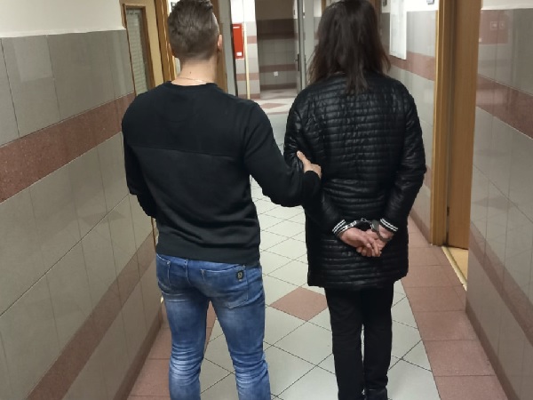 Policjant eskortujący skutego kajdankami podejrzanego korytarzem.