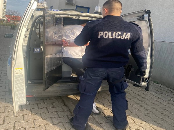 Policjant aresztujący podejrzanego w policyjnym furgonie. Na mundurze policjanta widać słowo „POLICJA”.