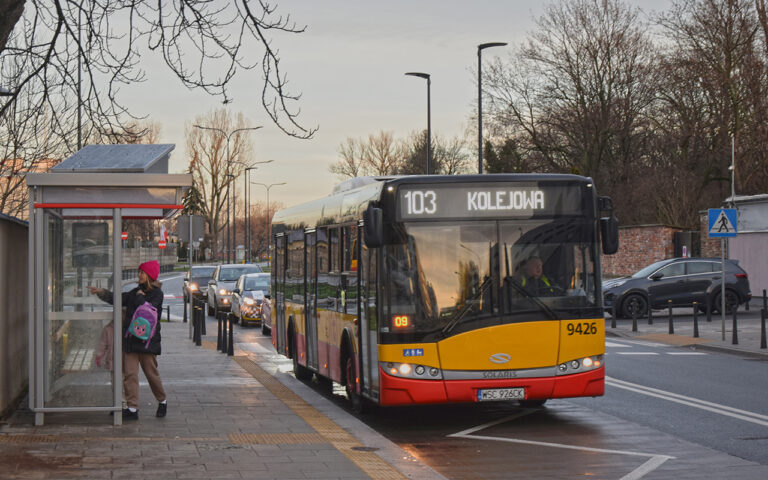 Kobieta czeka na przystanku autobusowym, przyjeżdża autobus miejski (linia 103 Kolejowa).