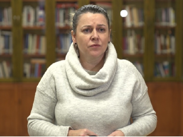 Kobieta w jasnoszarym golfie, poważny wyraz twarzy.