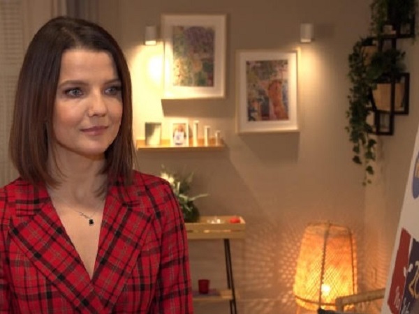 Kobieta w czerwonej kraciastej marynarce uśmiecha się do kamery.