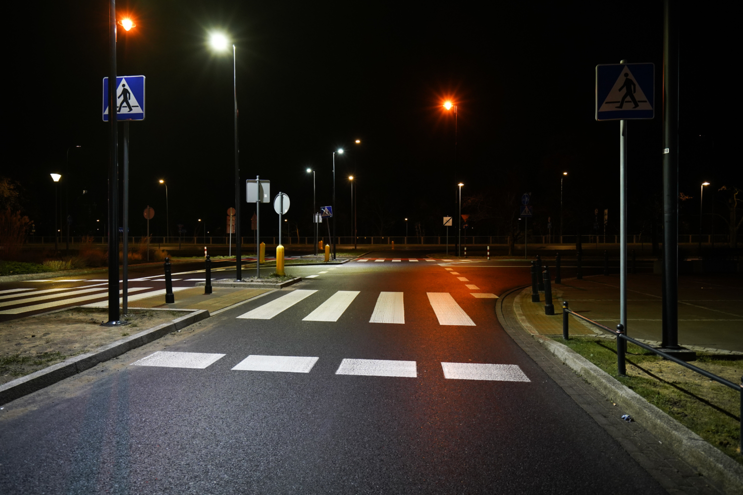Puste przejście dla pieszych nocą, oświetlone latarniami ulicznymi.