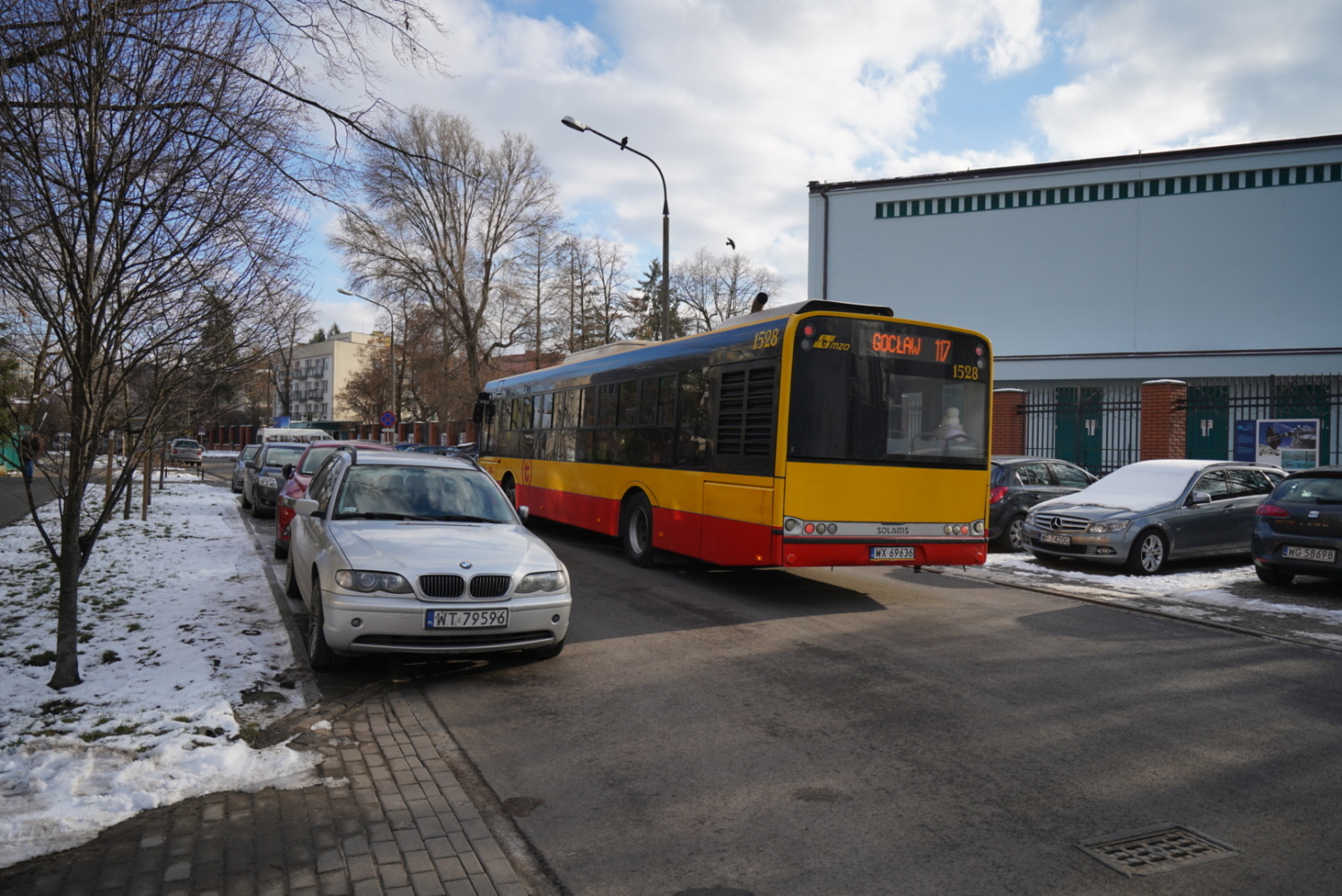 Autobus miejski na ulicy, zaparkowane samochody, zimowa sceneria