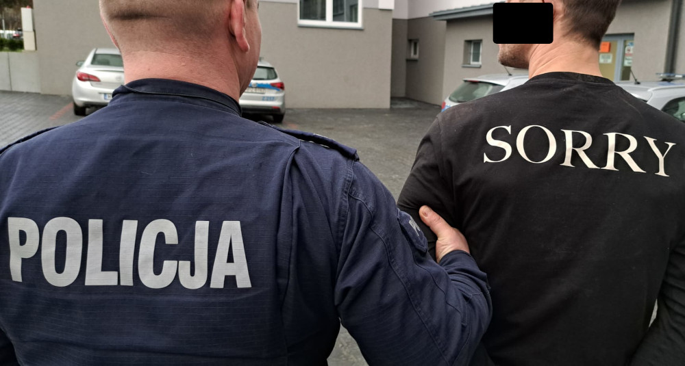 Policjant aresztujący mężczyznę, na którego koszulce widnieje napis „Przepraszam”