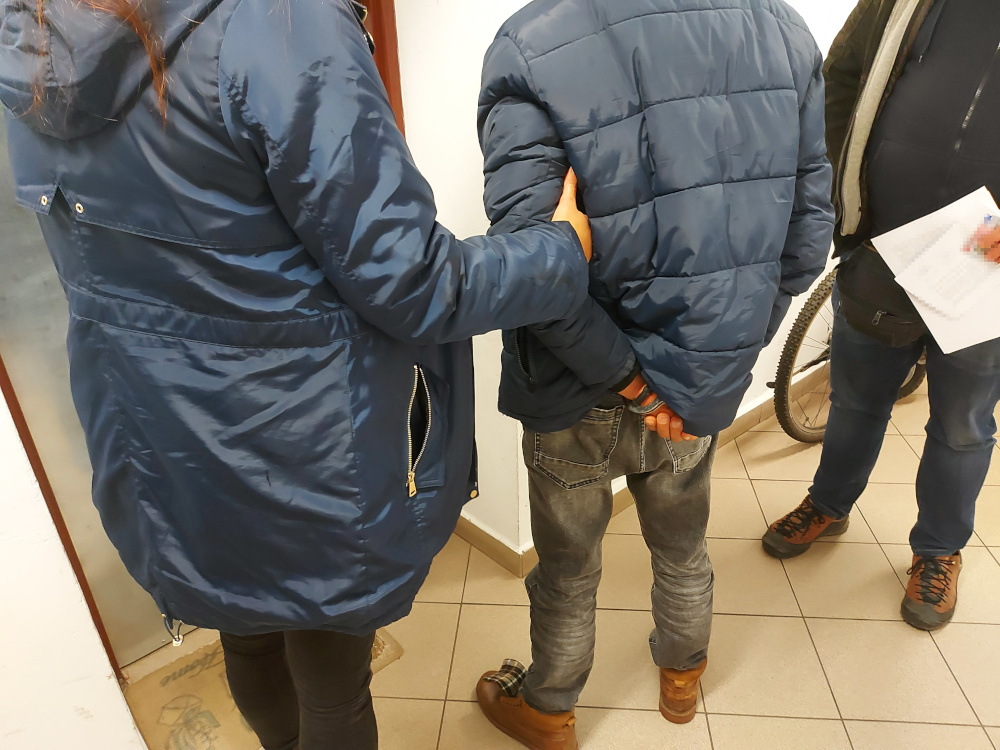 Policjanci zatrzymują podejrzanego, który miał ręce z tyłu.