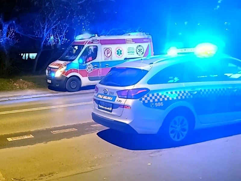 Pojazdy uprzywilejowane w nocy: karetka pogotowia i radiowóz z migającymi światłami.