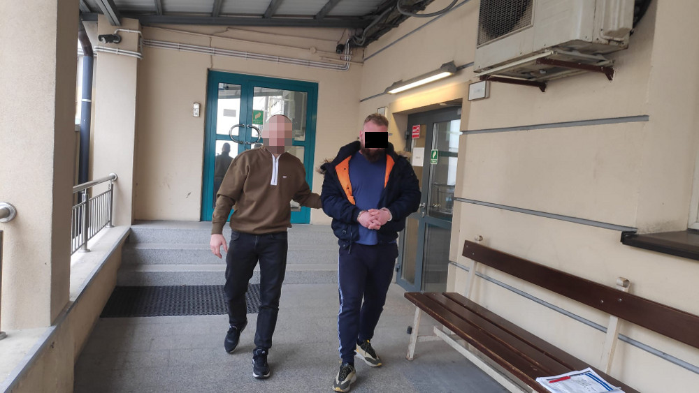 Policja eskortuje podejrzanego w kajdankach.