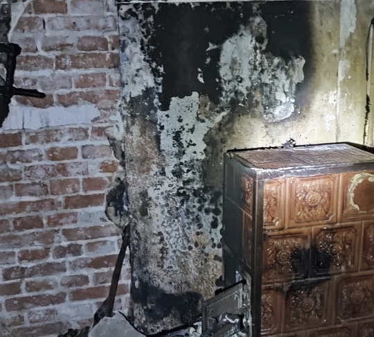 Uszkodzona przez ogień ściana z cegieł i piec kaflowy. Widoczne są uszkodzenia spowodowane dymem.