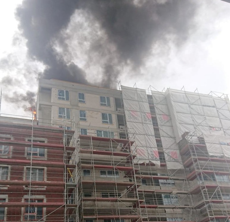 Z pożaru budynku w trakcie budowy wydobywa się dym, widoczne jest rusztowanie.