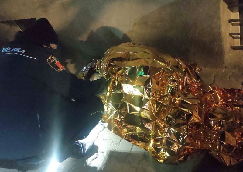 Ratownik udzielający pomocy osobie owiniętej w złoty koc termiczny.