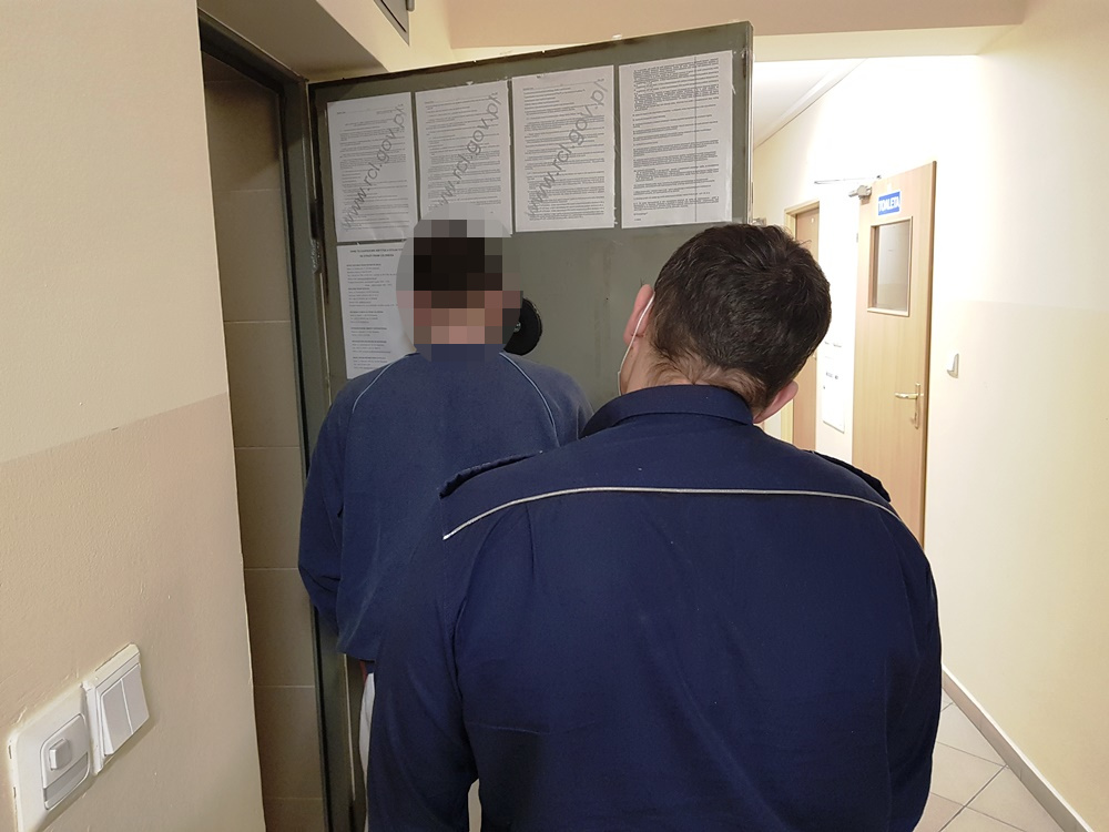 Policjant eskortujący podejrzanego przez drzwi.