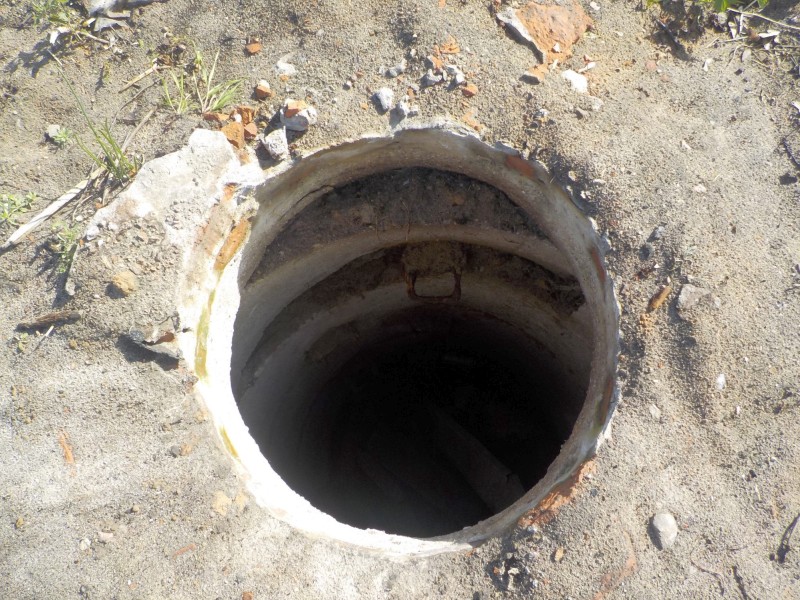 Zniszczona betonowa pokrywa studni odsłaniająca ciemny szyb