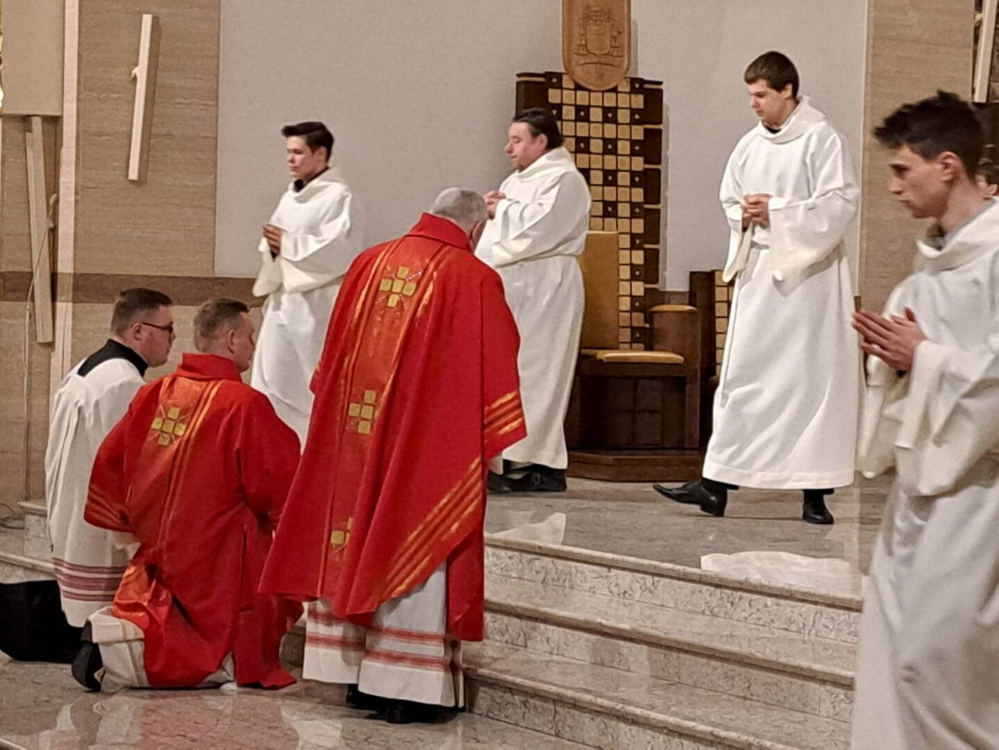 Księża katoliccy i ministranci w białych i czerwonych szatach podczas ceremonii religijnej.