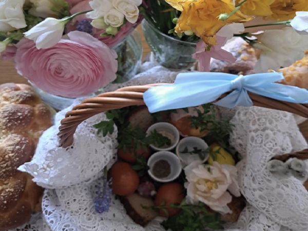 Koszyk wielkanocny wypełniony farbowanymi jajkami, chlebem i wiosennymi kwiatami.