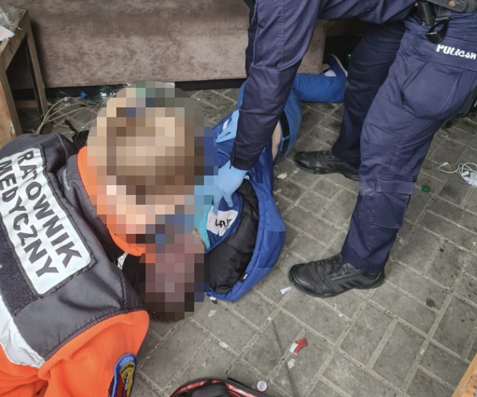 Ratownicy medyczni i policjanci udzielają pomocy rannemu leżącemu na ziemi.