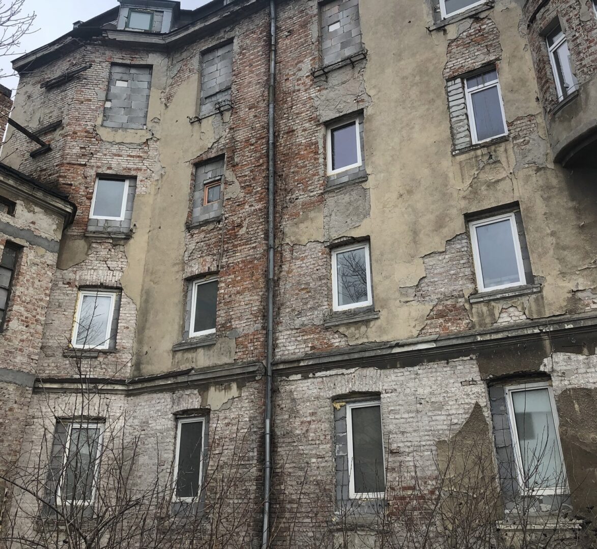Zniszczony budynek z cegły z wieloma oknami, noszący ślady zniszczenia i wymagający remontu.