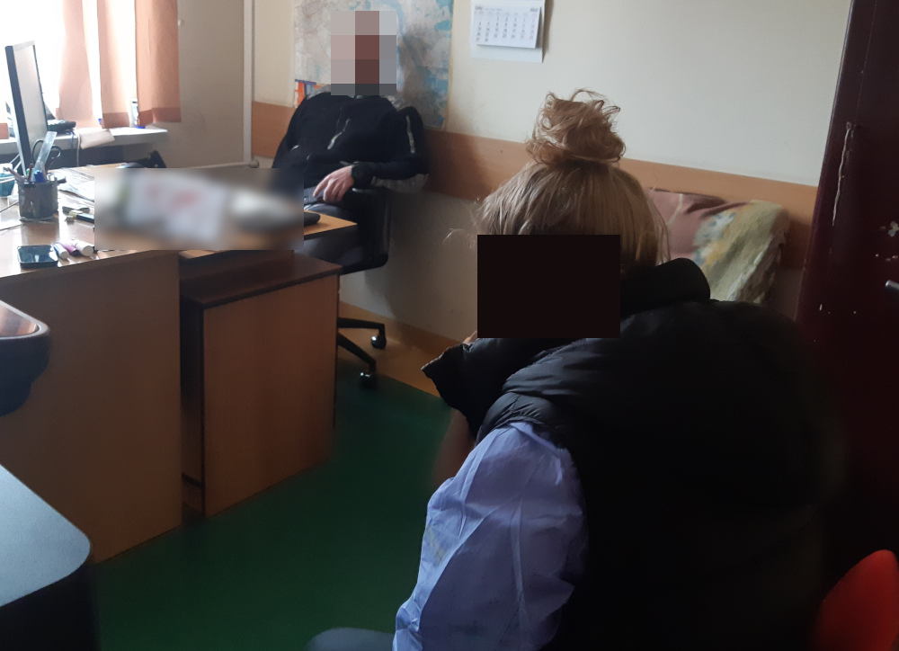 Kobieta w czarnej kamizelce siedzi naprzeciwko niewyraźnej osoby przy biurku i omawia jakąś sprawę.