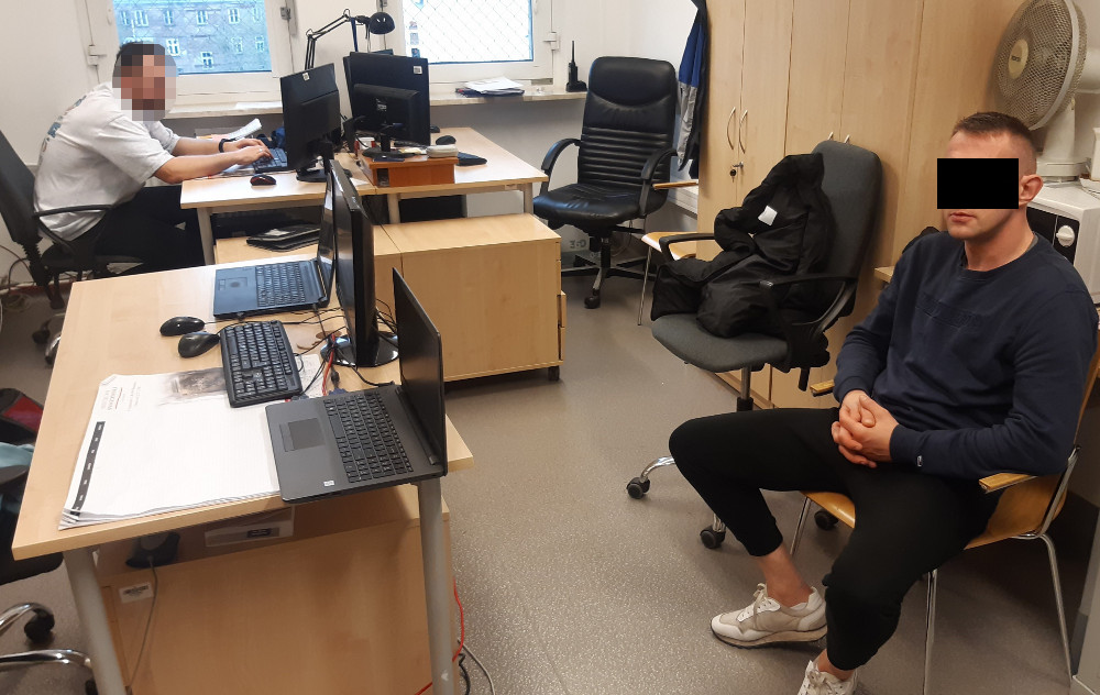 Dwóch mężczyzn w biurze, jeden pracuje przy komputerze, drugi siedzi naprzeciwko kamery.