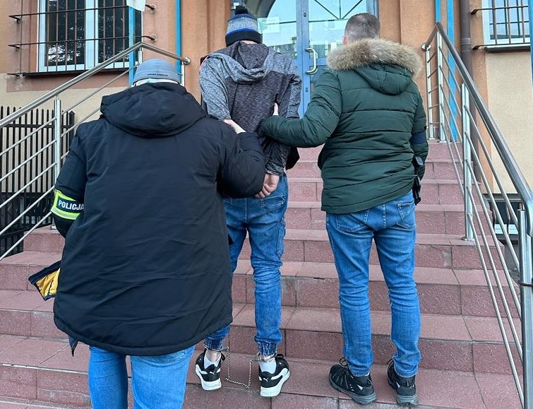 Policjanci eskortują podejrzanego w kajdankach po schodach sądu.