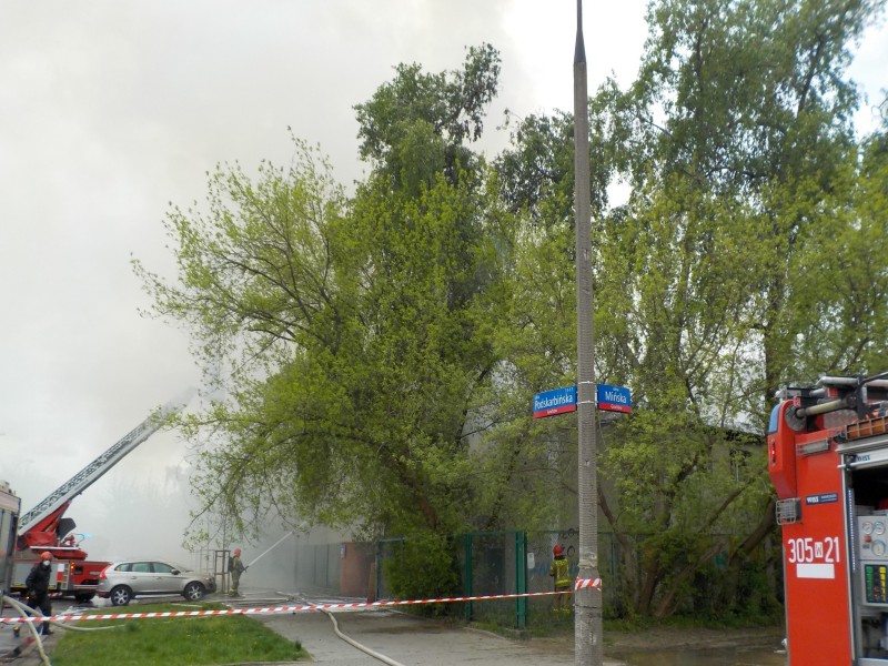 Strażacy gaszą pożar budynku za pomocą wozu drabinowego. Z budynku wydobywa się dym.