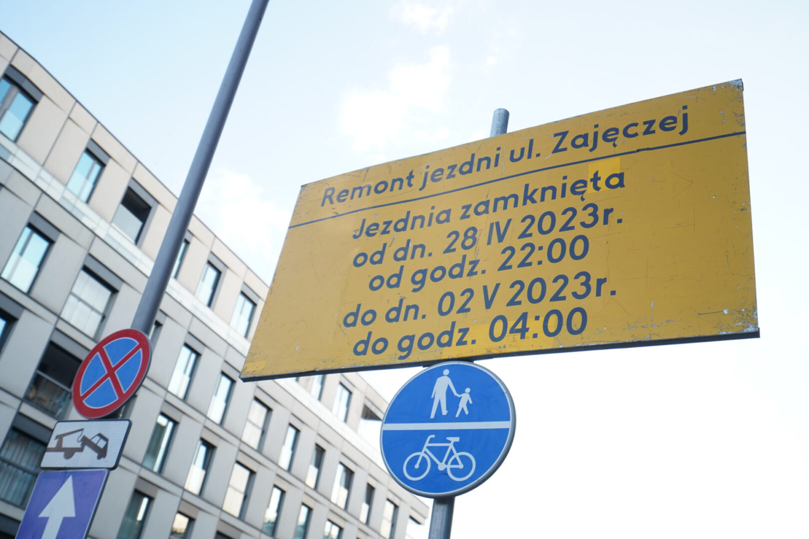 Znak zamknięcia drogi w języku polskim: „Remont jezdni ul. Zajęczej”, oznaczający zamknięcie od 28 kwietnia, godz. 22:00 do 2 maja, godz. 04:00. Symbol wspólnej ścieżki dla pieszych i rowerzystów.