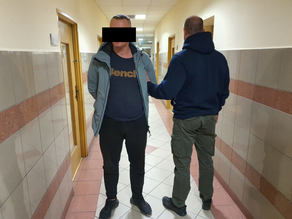 Policjant eskortujący podejrzanego korytarzem.