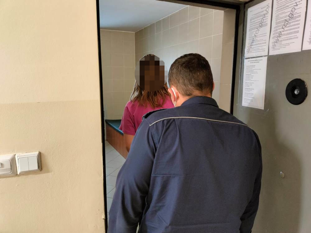 Policjant eskortujący zatrzymaną osobę przez drzwi.