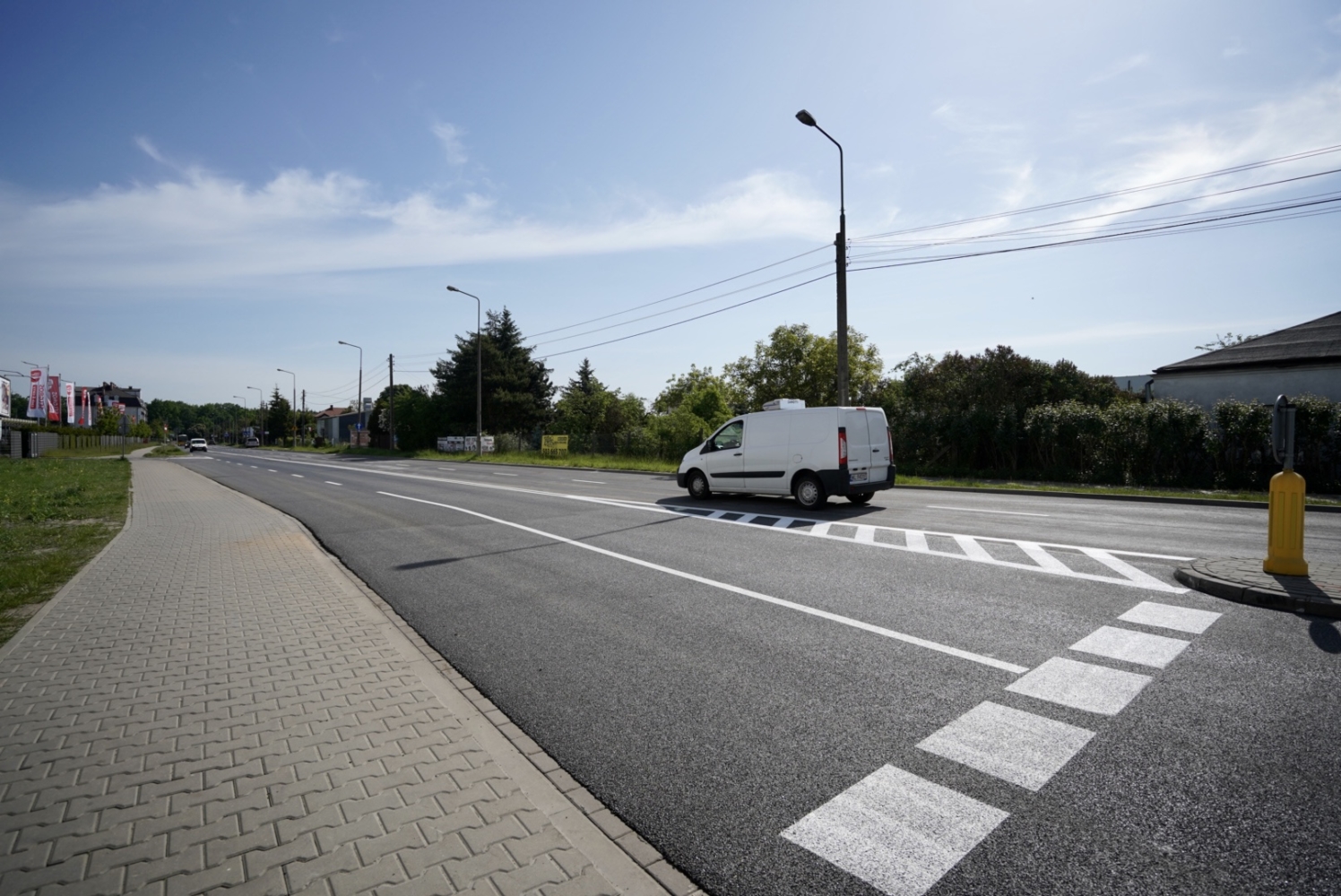 Biały samochód dostawczy na ulicy osiedlowej z przejściem dla pieszych